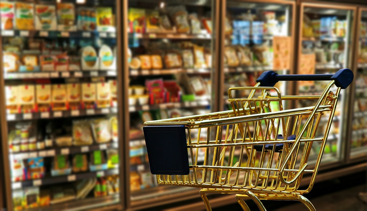 Bild eines goldenen Einkaufswagens vor Kühlregalen in einem Supermarkt